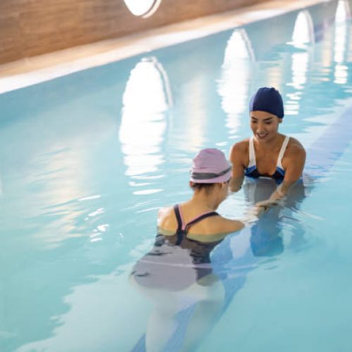 Happy physical therapist helping an injured woman doing her recovery exercises in hydrotherapy - physical therapy concepts